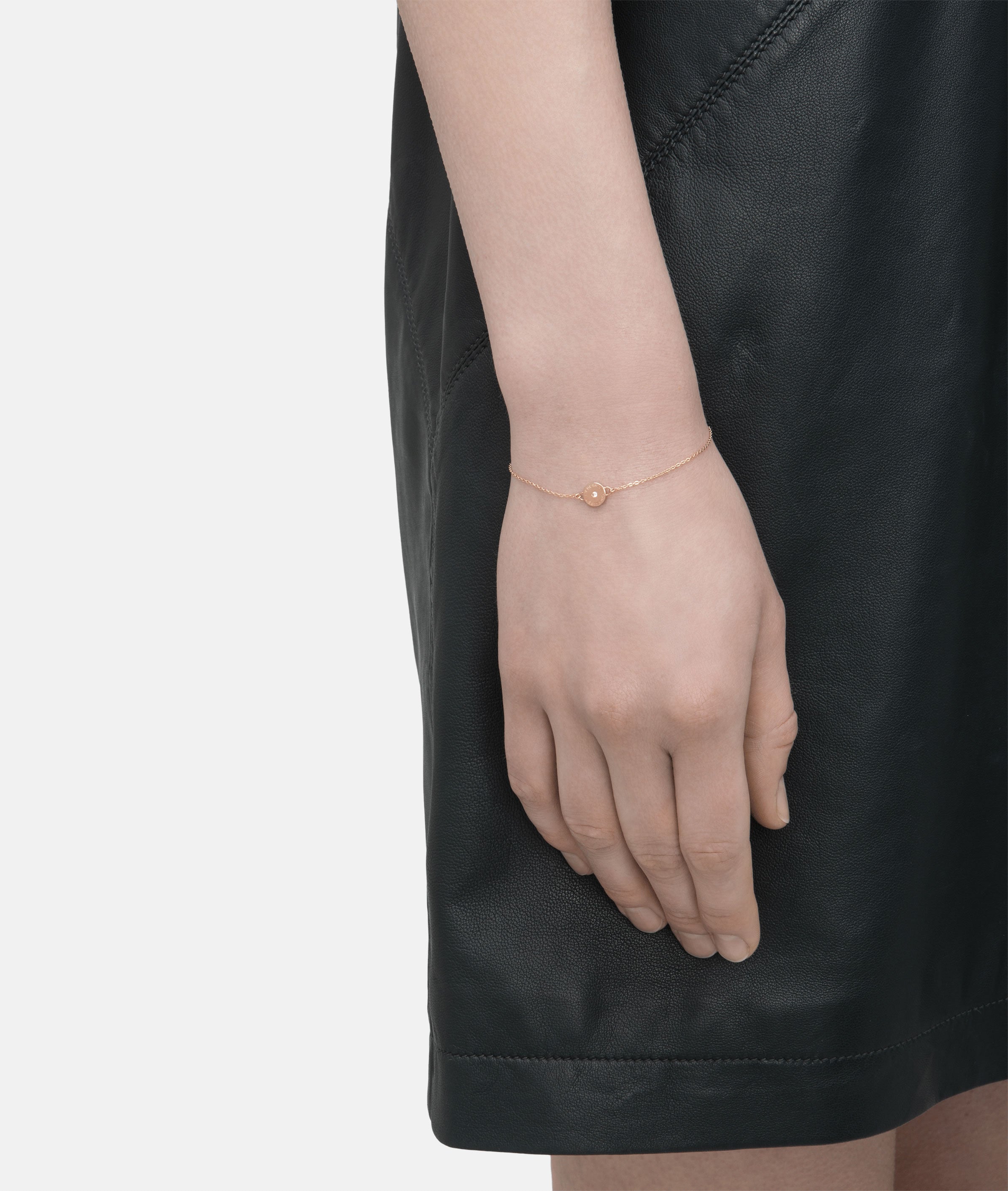 Eine Person trägt ein schwarzes Kleid und das Liebeskind Berlin LIEBESKIND BERLIN Set - Sparkling Rosé, bestehend aus einem zarten Roségoldarmband mit einem kleinen runden Anhänger, an ihrem Handgelenk.
