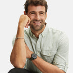 Mann mit kurzen braunen Haaren, lächelnd, trägt ein hellgrünes Fynch-Hatton-Button-up-Hemd und das Fynch-Hatton-Armband - The Twist an seinem Handgelenk, posiert mit der Hand am Kinn.