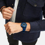 Eine Person, die die Fynch-Hatton Armbanduhr - The Blue Chrono und eine marineblaue Jacke trägt, steht mit einer Hand an ihrem Ärmel.