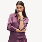 Eine Frau in einem seidigen lila Kleid posiert selbstbewusst mit der Hand am Kinn und präsentiert die LIEBESKIND BERLIN Armbanduhr - Glitter-Special von Liebeskind Berlin vor einem schlichten weißen Hintergrund.