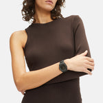 Eine Frau in einem braunen einärmeligen Kleid posiert und präsentiert die Liebeskind Berlin Armbanduhr - Vintage Classic mit einem eleganten Edelstahlgehäuse am linken Arm.