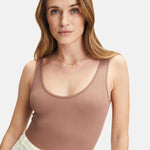 Frau in einem ärmellosen lila gerippten Tank-Top und einer zarten Tamaris Halskette - Coin von Tamaris, stehend vor einem weißen Hintergrund.