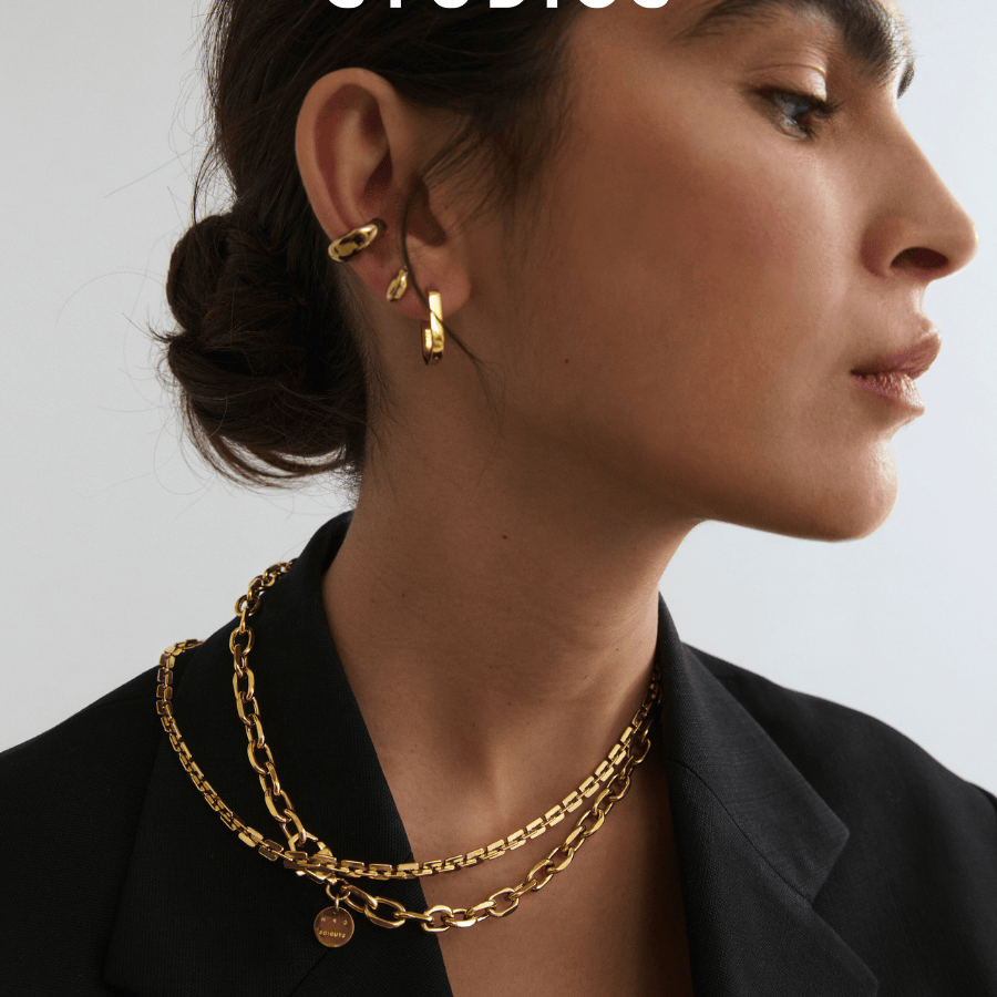  zur ersten Schmuck- und Uhrenkollektion von COPENHAGEN STUDIOS – stilvolles Portrait einer Frau mit goldenen Statement-Ohrringen und Layering-Ketten, kombiniert mit einem eleganten schwarzen Blazer.