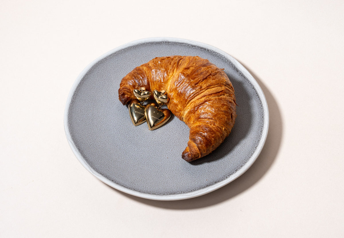COPENHAGEN STUDIOS Puffy Heart Ohrstecker neben einem frischen Croissant