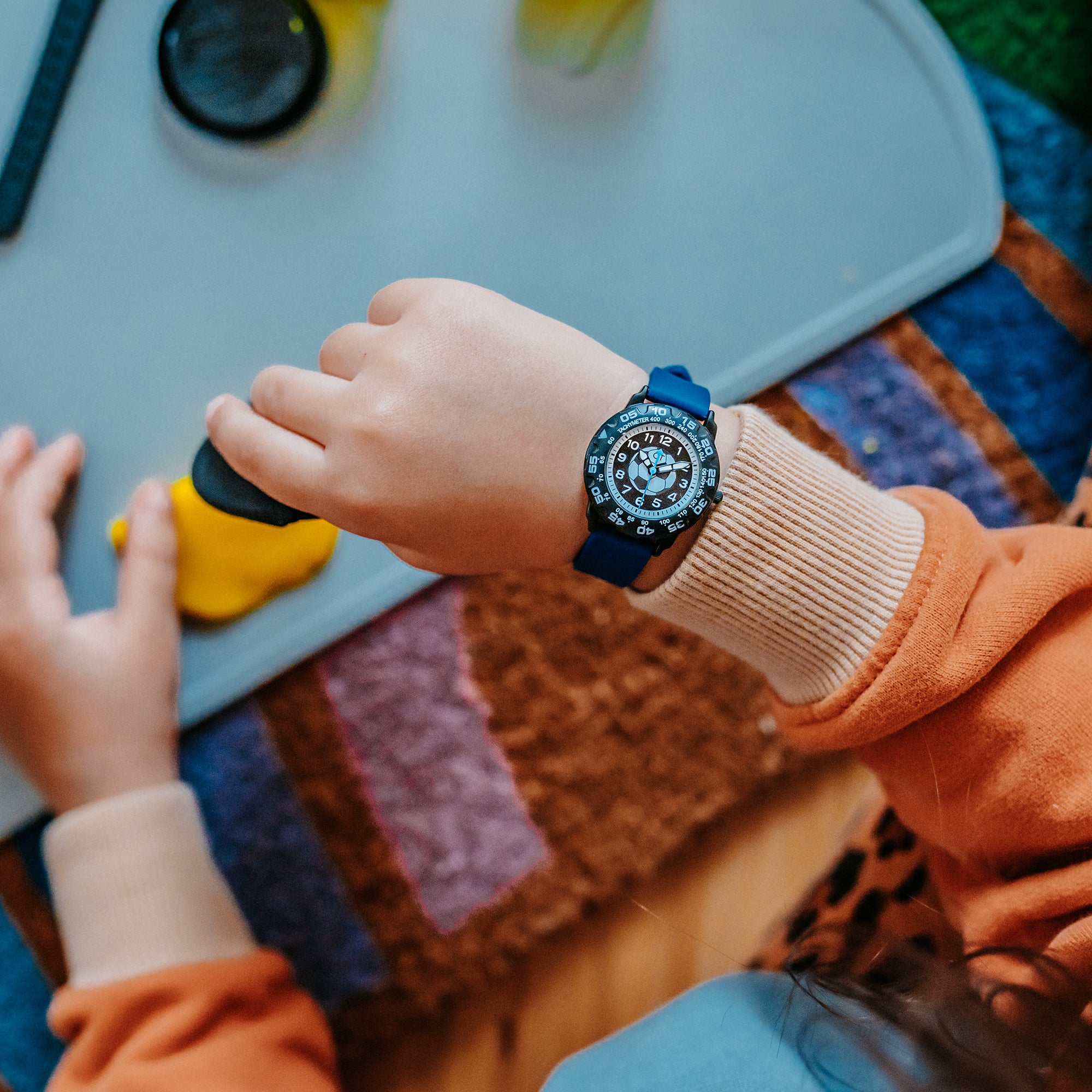 Kind mit blauer Fußball-Kinderuhr beim Spielen am Tisch – robuste Uhr für aktive Jungen im Alltag und bei kleinen Abenteuern.