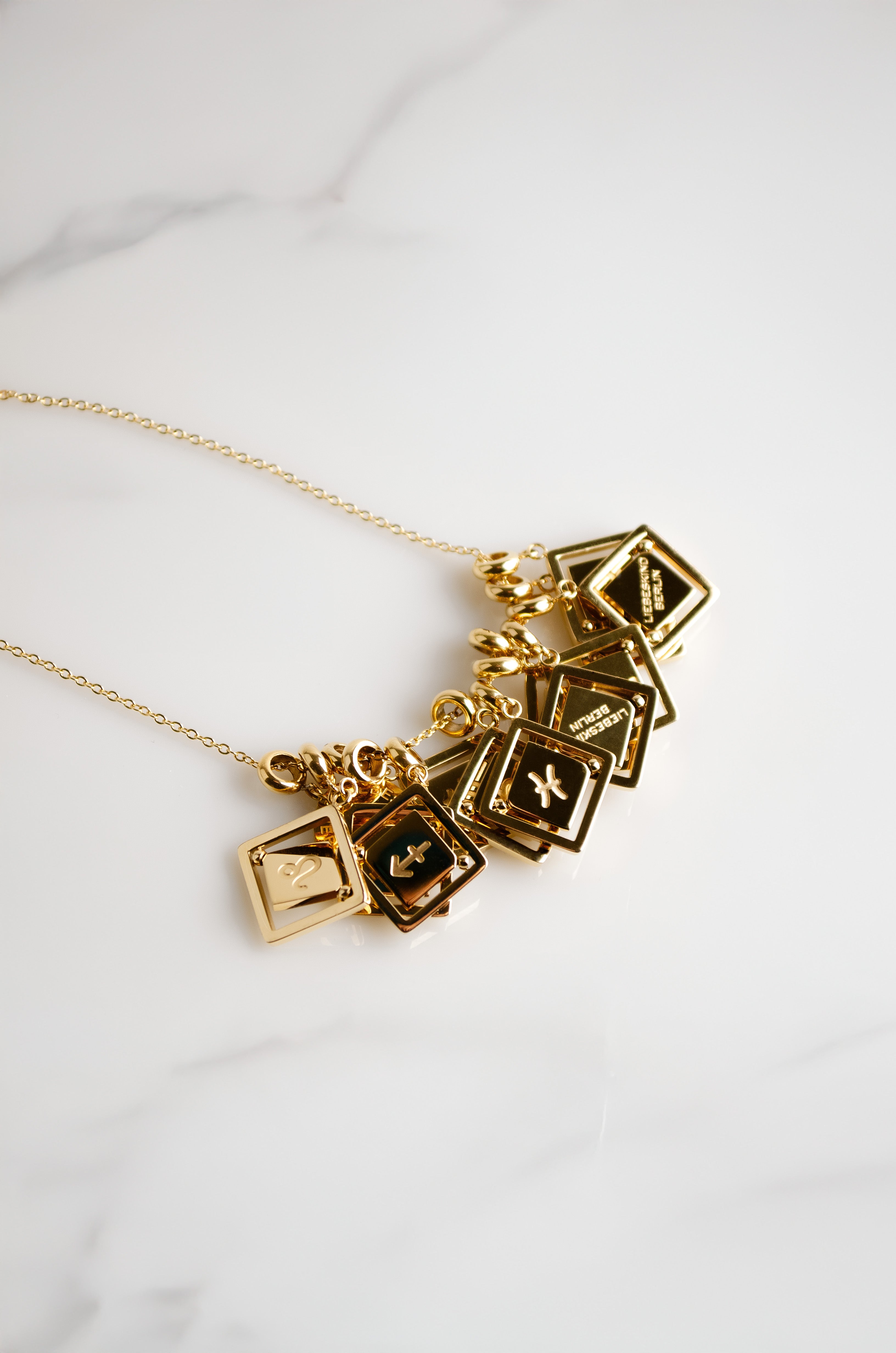 Alle Sternzeichen Charms von LIEBESKIND BERLIN an einer Kitte in Gold auf Marmor untergrund