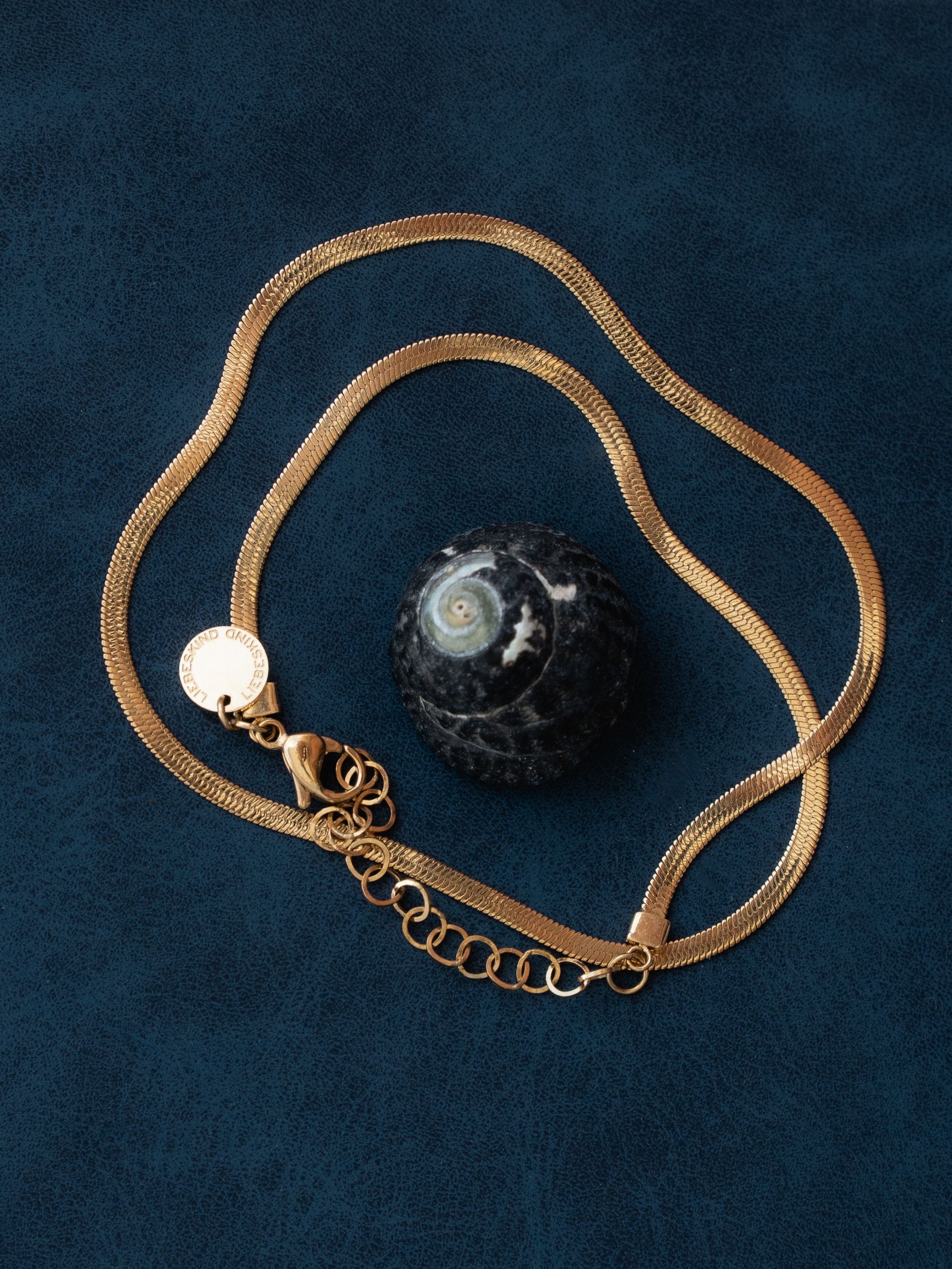 Goldfarbene LIEBESKIND BERLIN The Sleek Halskette auf dunkelblauem Hintergrund mit Muschel – sommerliche Schmuck-Inspiration zum End of Summer Sale