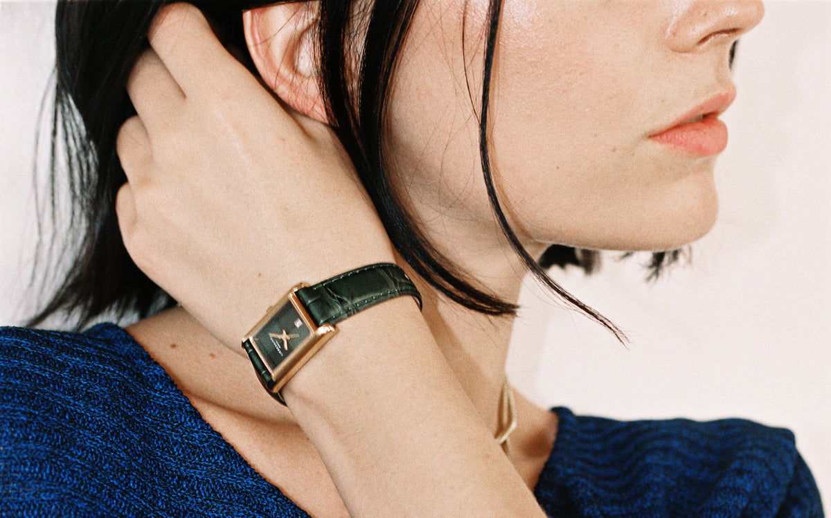 LIEBESKIND BERLIN rechteckige Armbanduhr mit dunklem Lederarmband und goldfarbenem Gehäuse am Handgelenk eines Models