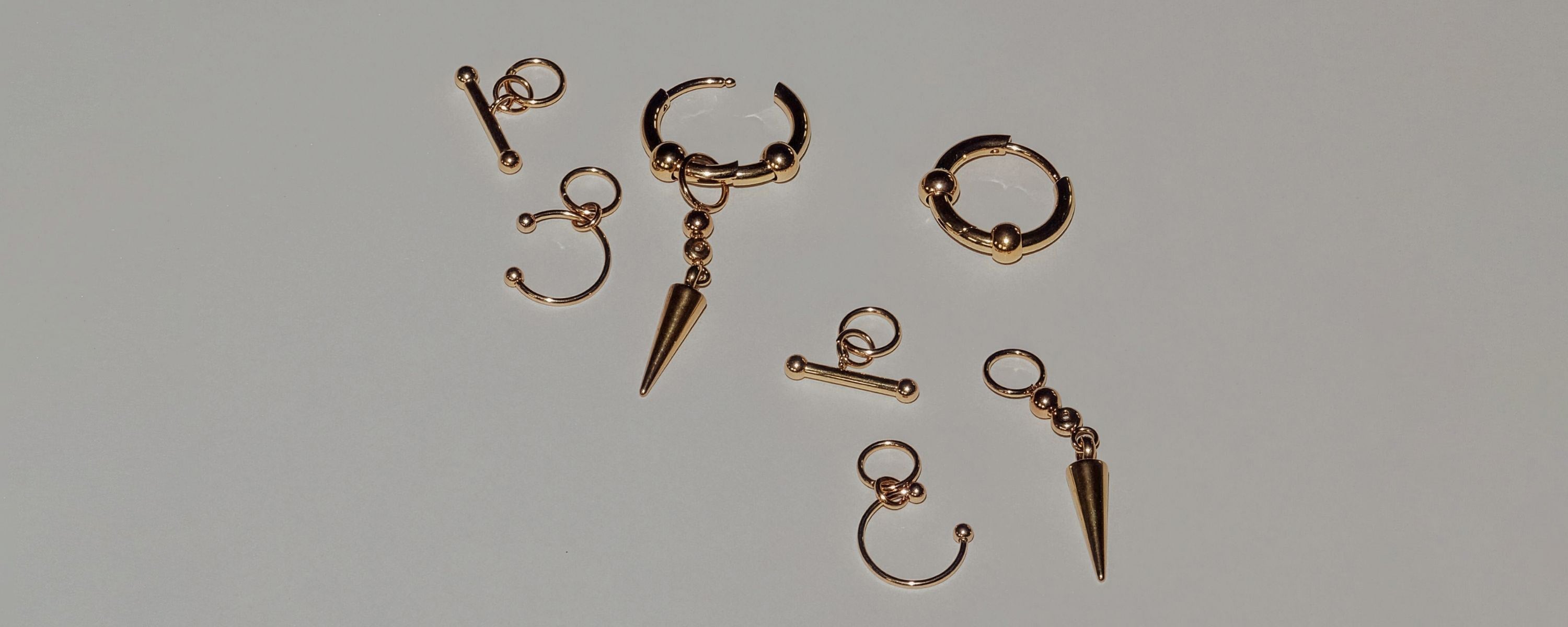 LIEBESKIND BERLIN Ohrringe in Goldoptik mit Kugel- und Spike-Anhänger, Creolen und Ear Cuffs modern arrangiert auf hellem Hintergrund – markanter Statement-Schmuck.