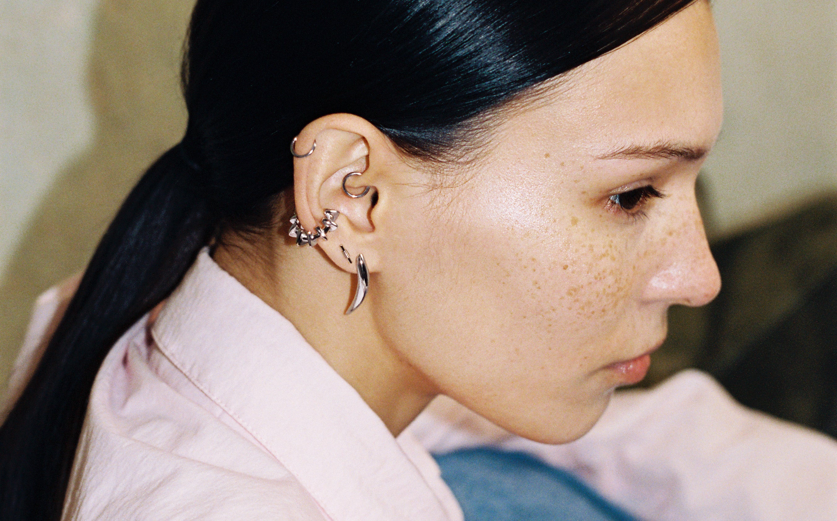 Seitenprofil eines Models mit mehreren silberfarbenen Ohrringen von LIEBESKIND BERLIN, darunter Creolen und Ear Cuffs – urbaner, minimalistischer Schmucklook.