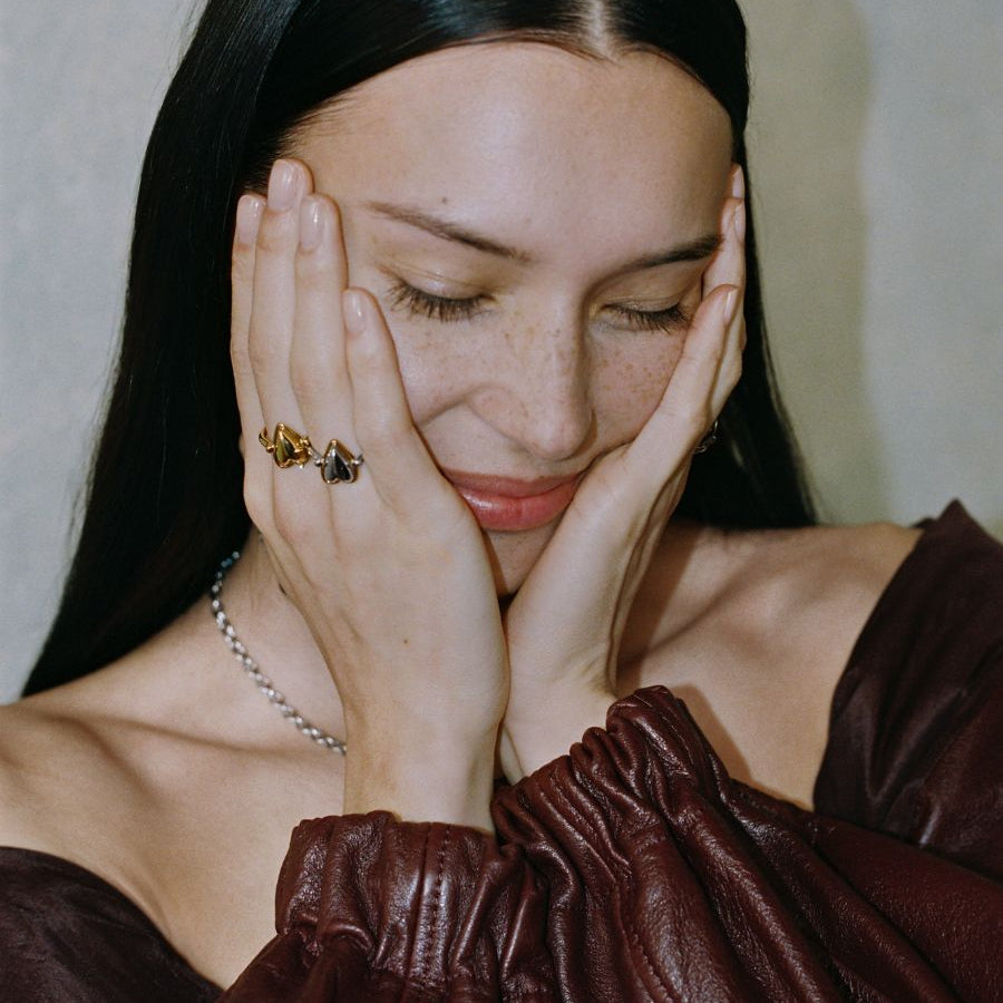 Model trägt LIEBESKIND BERLIN Ringe im Bicolor-Design und zarte Halskette, mit geschlossenen Augen und Händen im Gesicht – moderner, femininer Schmucklook.
