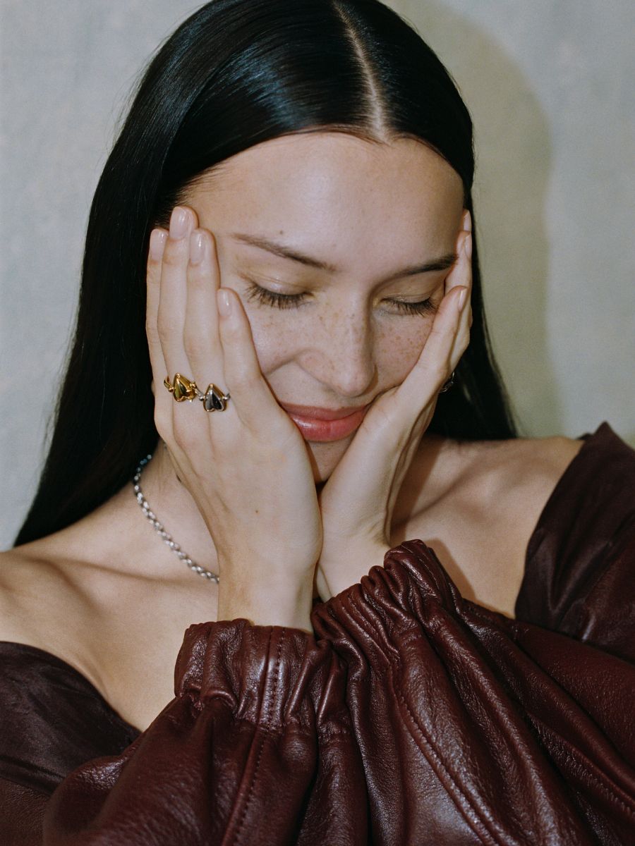 Model trägt LIEBESKIND BERLIN Ringe im Bicolor-Design und zarte Halskette, mit geschlossenen Augen und Händen im Gesicht – moderner, femininer Schmucklook.