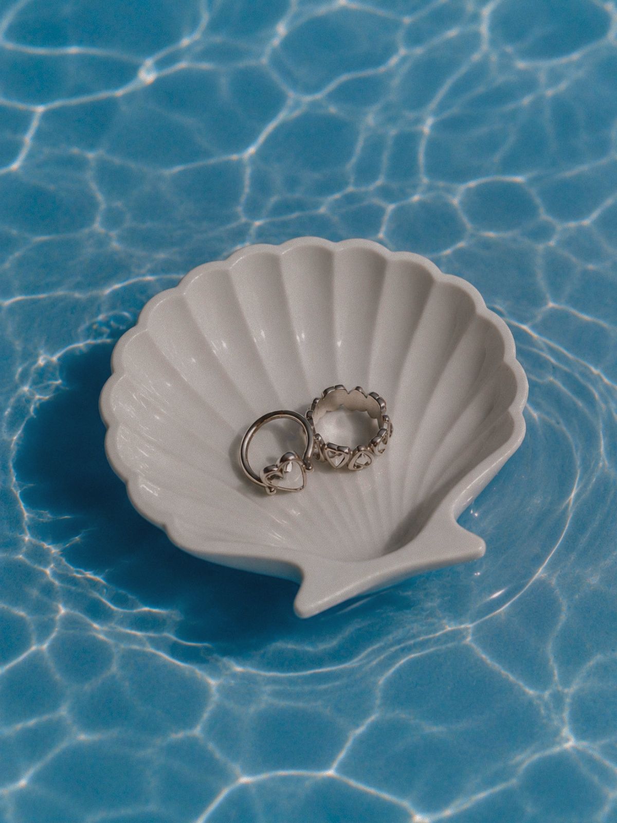 Silberfarbene Herzringe von LIEBESKIND BERLIN in muschelförmiger Schale auf schimmerndem Wasser – inspiriert von Summer Styles.