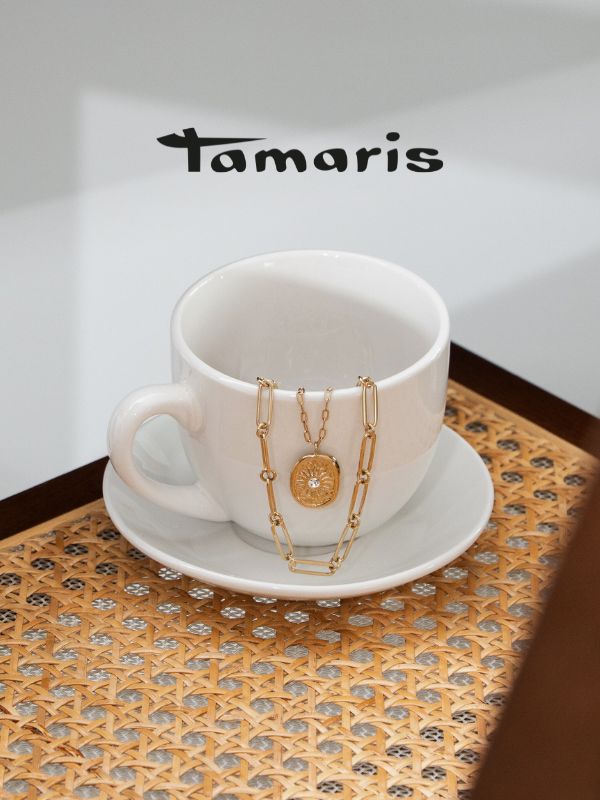 Tamaris Halskette mit strukturiertem Anhänger in Goldoptik, dekorativ über einer weißen Tasse auf Rattan-Untergrund inszeniert – moderner, eleganter Schmucklook.