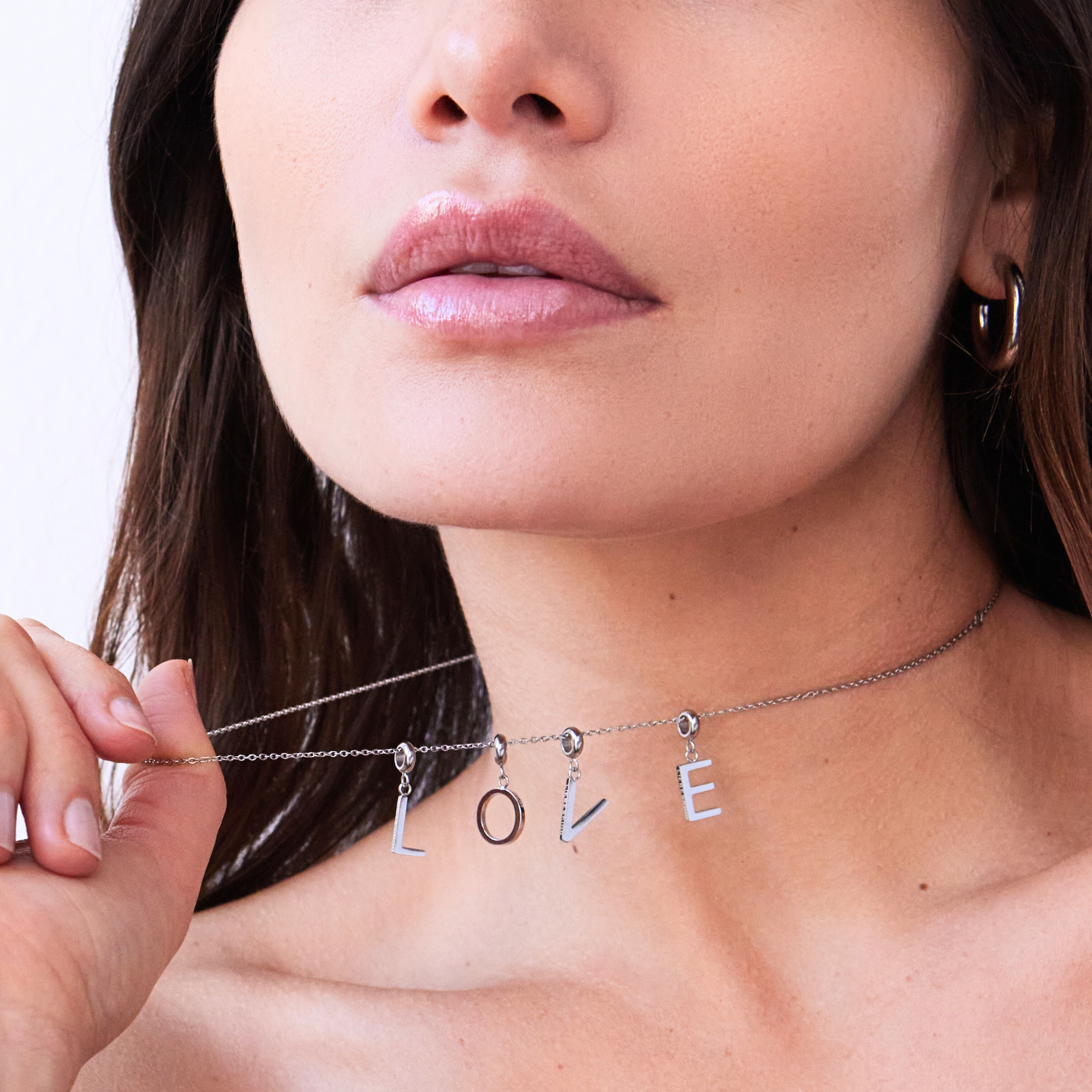 Frau hält eine silberne Halskette mit Anhängern, die das Wort ‚LOVE‘ bilden, nah am Hals.