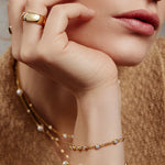 Eine Frau trägt Goldschmuck mit Perlen und Diamanten, darunter das Armband Ania Haie Armband - Round Stone von Ania Haie, sowie einen Ring und mehrlagige Halsketten.