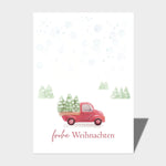 Die "Postkarte - Frohe Weihnachten DIN A6" von Cool | Time zeigt einen roten Lastwagen mit Weihnachtsbäumen in einer verschneiten Landschaft, darunter der Text "Frohe Weihnachten".