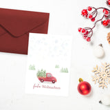 Postkarte in A6 mit süßem Weihnachtsmotiv - ein kleines Auto transportiert Weihnachtsbäume und darunter steht "frohe Weihnachten"