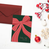 Postkarte in A6 mit süßem Weihnachtsmotiv - Eine große rote Schleife auf grünem Untergrund mit dem Text "Frohes Fest und alles Liebe und Gute im neuen Jahr"