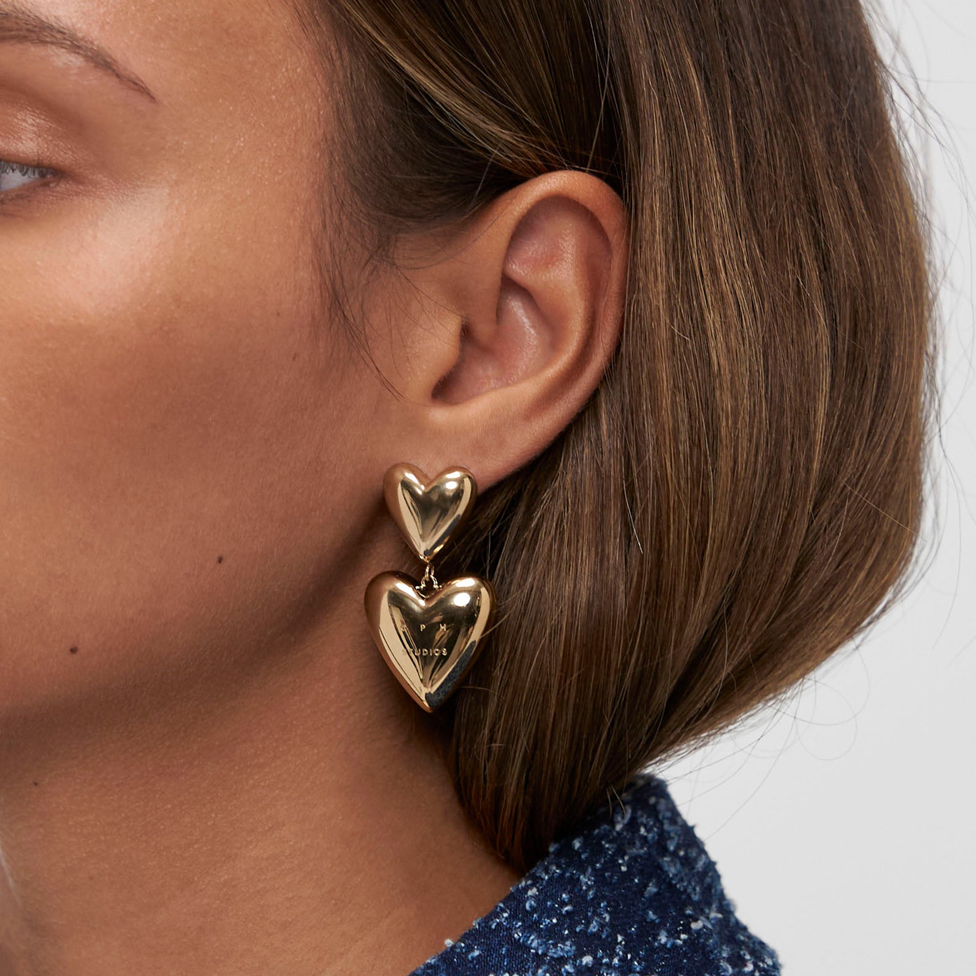Nahaufnahme eines Frauenohrs mit kurzen braunen Haaren, das Ohrstecker von Copenhagen Studios trägt - Puffy Hearts Ohrringe - eine elegante Note von Copenhagen Studios.