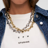 Nahaufnahme von zwei metallischen Herzketten, eine goldene und eine silberne, gestylt auf einem weißen Hemd - und die COPENHAGEN STUDIOS Halskette - Puffy Hearts by Copenhagen Studios mit ihrem eleganten Herzkarabiner-Detail hervorhebend.