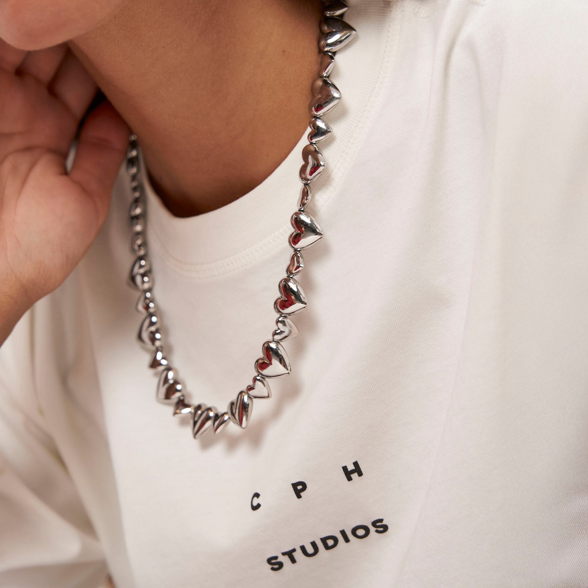 Eine Person trägt die COPENHAGEN STUDIOS Halskette - Puffy Hearts von Copenhagen Studios und ein weißes Copenhagen Studios T-Shirt.