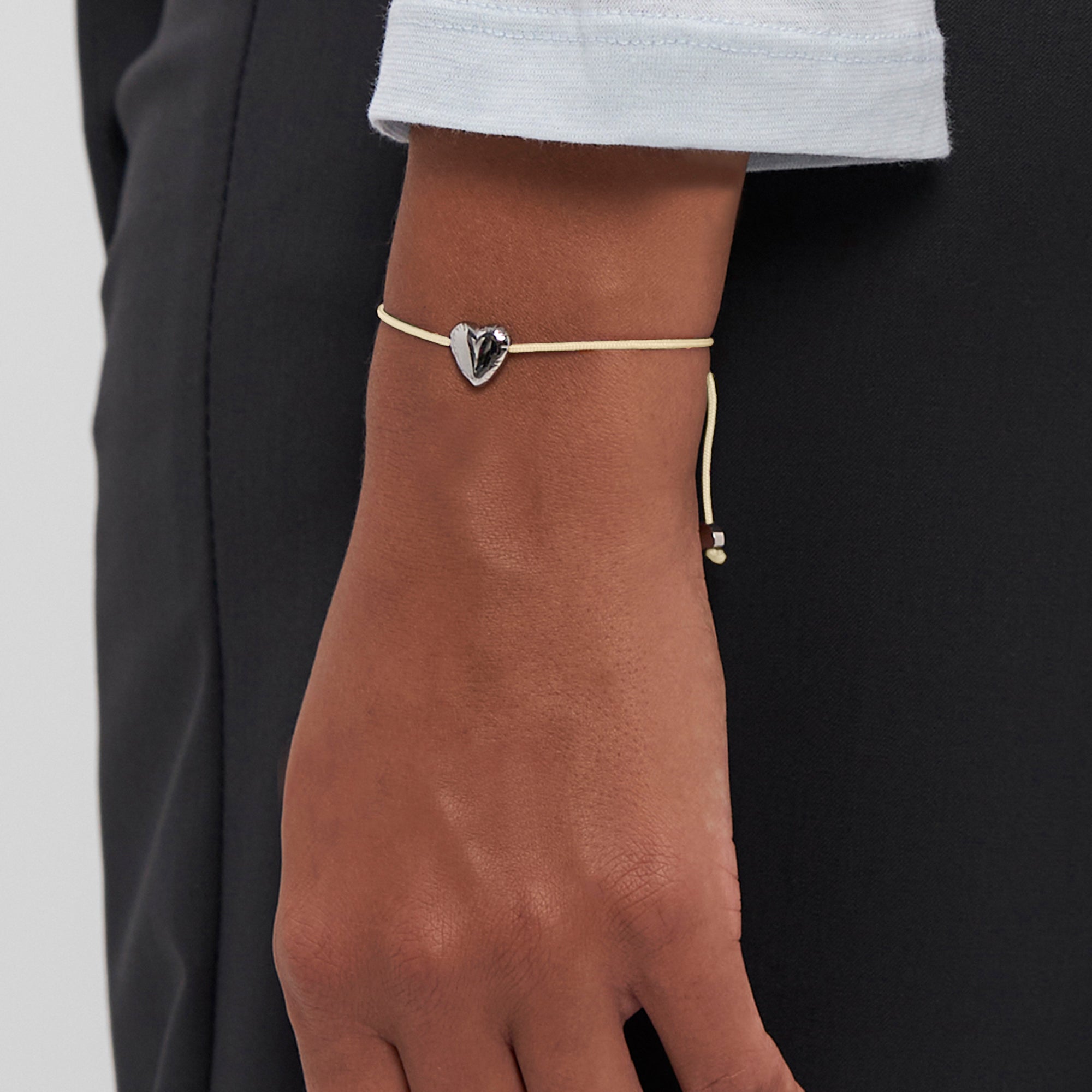 Nahaufnahme einer Hand, die das Copenhagen Studios COPENHAGEN STUDIOS Armband - Balloon Hearts trägt. Der zarte metallische Herzanhänger sorgt für einen eleganten Touch.