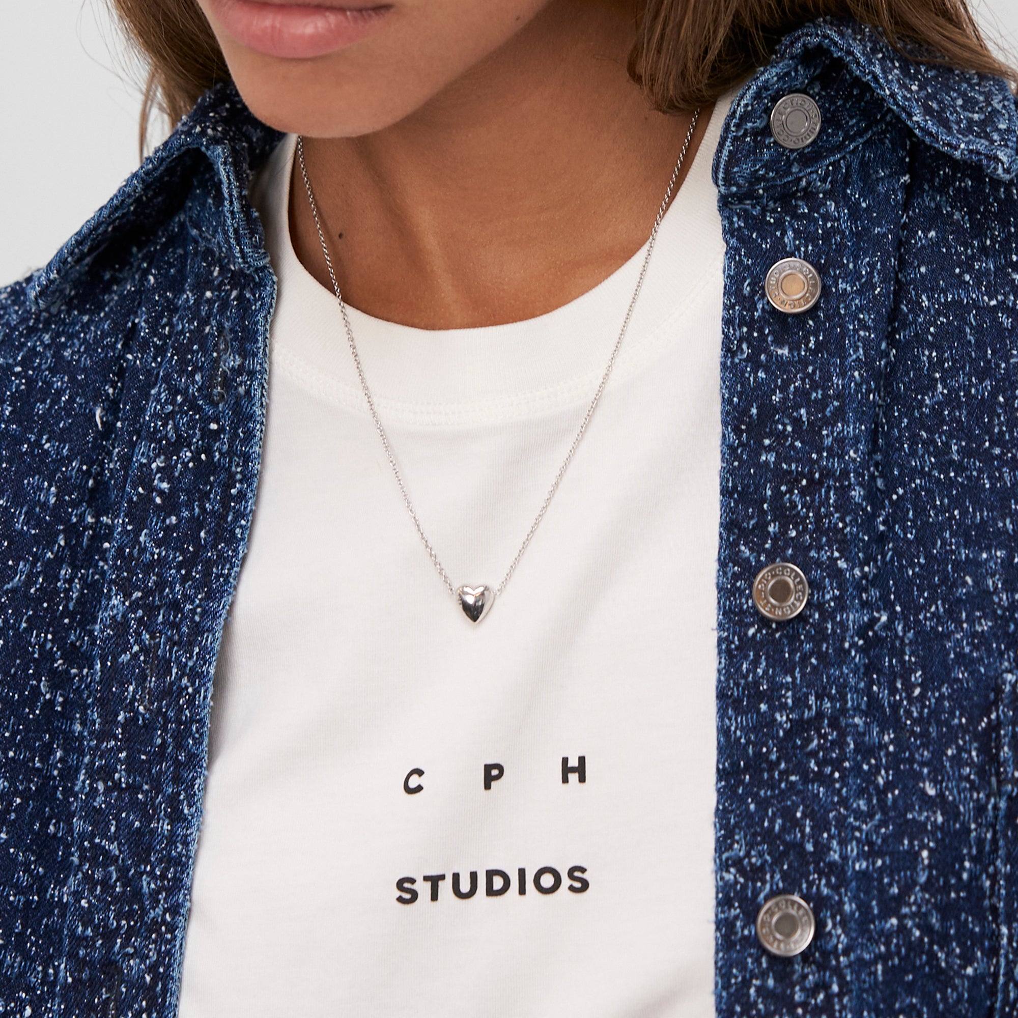 Frau trägt eine blaue Jeansjacke, ein weißes Hemd und die COPENHAGEN STUDIOS Halskette - Balloon Hearts by Copenhagen Studios - eine elegante filigrane Halskette mit einem herzförmigen Anhänger.