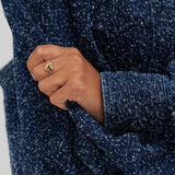 Eine Hand, die den Copenhagen Studios COPENHAGEN STUDIOS Ring - Balloon Hearts trägt, hält den Ärmel eines strukturierten, dunkelblau gesprenkelten Mantels und verleiht dem Ring einen Hauch von moderner Eleganz.