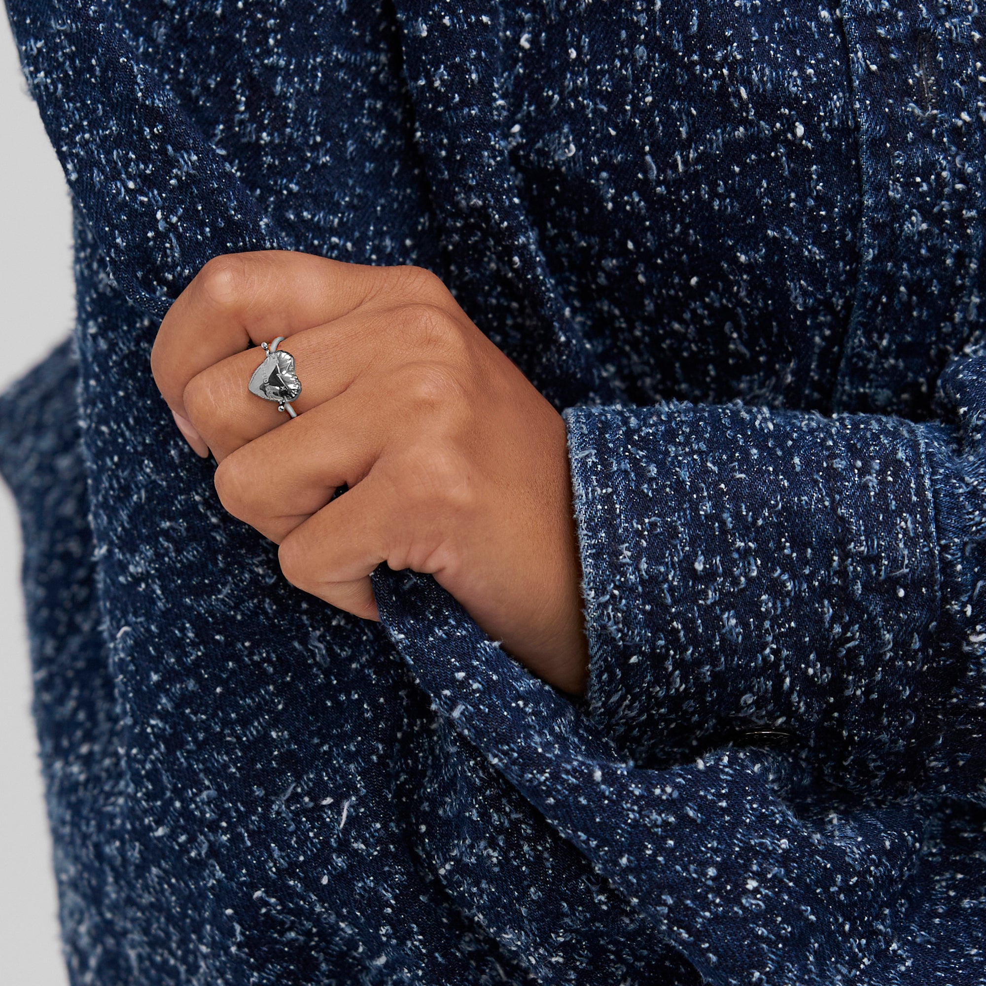 Eine Hand, die den Ring "Balloon Hearts" von Copenhagen Studios trägt, hält den Ärmel einer blau-weiß strukturierten Jacke.