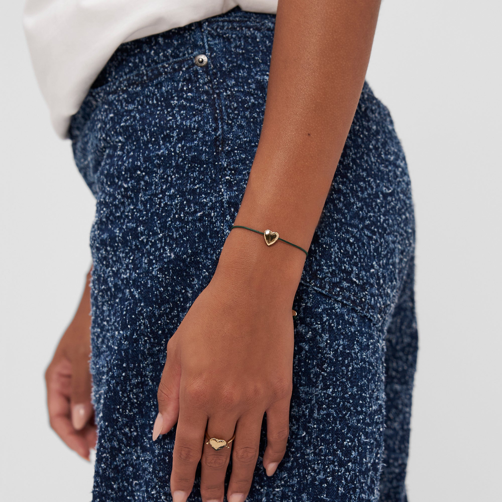 Eine Person trägt eine blaue Jeans, ein Copenhagen Studios Armband - Balloon Hearts mit einem goldenen Herzanhänger und einen passenden goldenen Herzring.
