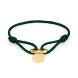 Das COPENHAGEN STUDIOS Armband - Fabric Link von Copenhagen Studios zeichnet sich durch eine grüne Kordel, einen goldenen runden Anhänger und einen goldenen Verschluss in der Mitte aus, der das charakteristische Armbanddesign der Marke widerspiegelt.
