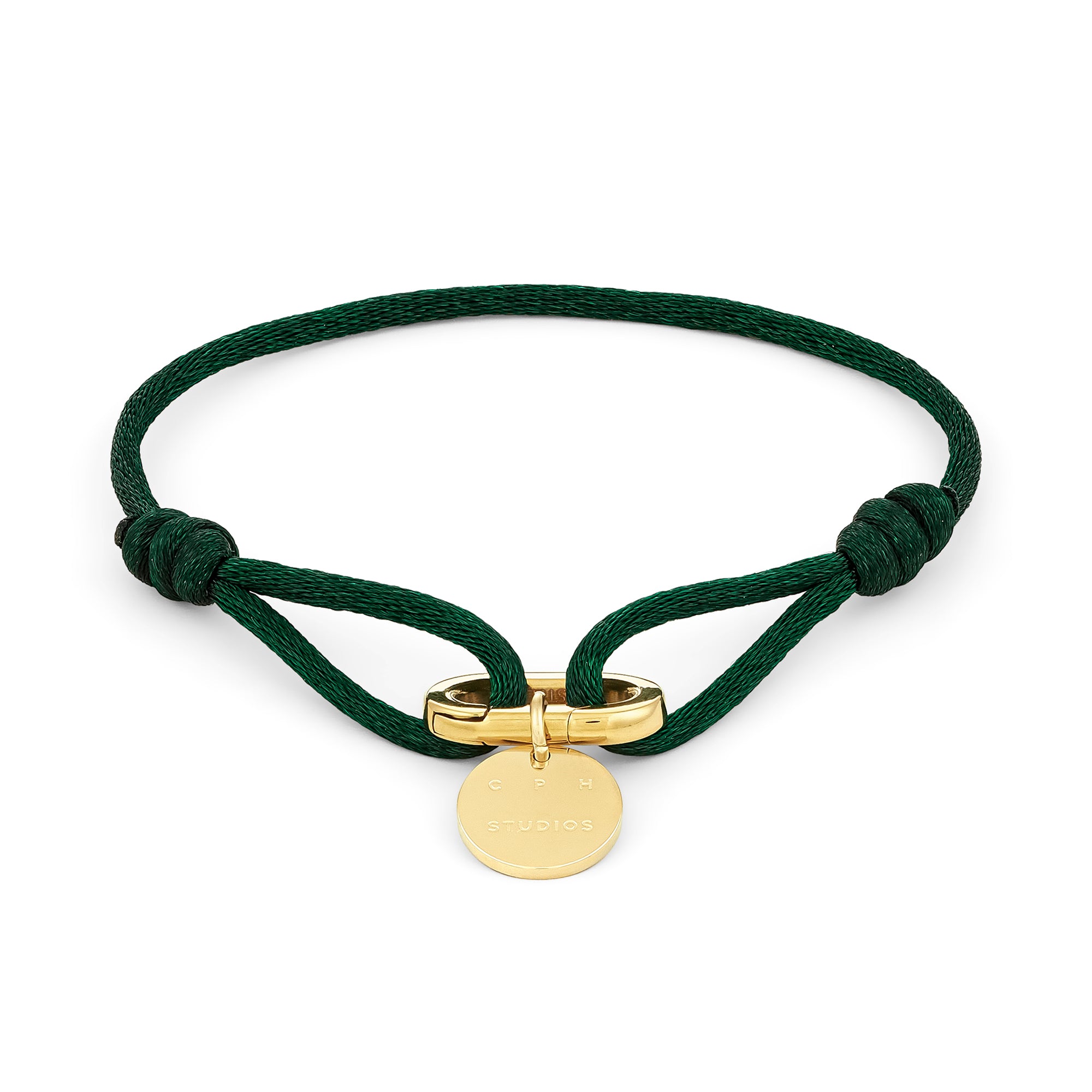 Das COPENHAGEN STUDIOS Armband - Fabric Link von Copenhagen Studios zeichnet sich durch eine grüne Kordel, einen goldenen runden Anhänger und einen goldenen Verschluss in der Mitte aus, der das charakteristische Armbanddesign der Marke widerspiegelt.