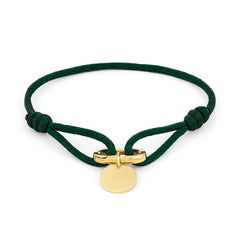 Das COPENHAGEN STUDIOS Armband - Fabric Link von Copenhagen Studios zeichnet sich durch eine grüne Kordel, einen goldenen runden Anhänger und einen goldenen Verschluss in der Mitte aus, der das charakteristische Armbanddesign der Marke widerspiegelt.