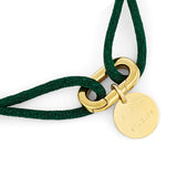Das COPENHAGEN STUDIOS Armband - Fabric Link von Copenhagen Studios zeigt einen goldenen Anhänger mit eingraviertem Text an einer grünen, geflochtenen Kordel und einem großen, goldenen Glied und besticht durch modernes, elegantes Design.