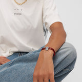 Person in blauer Jeans und weißem T-Shirt trägt im Schneidersitz ein Copenhagen Studios Armband - Fabric Link mit einem runden Anhänger.