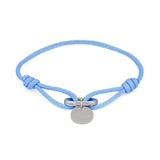 Das COPENHAGEN STUDIOS Armband - Fabric Link von Copenhagen Studios besteht aus einem hellblauen Stoffarmband mit einem runden silbernen Anhänger und einem Metallverschluss in der Mitte.