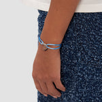 Jemand trägt das COPENHAGEN STUDIOS Armband - Fabric Link, ein hellblaues Armband mit einem runden silbernen Anhänger, gepaart mit einer blauen strukturierten Hose - ein elegantes Accessoire von Copenhagen Studios.
