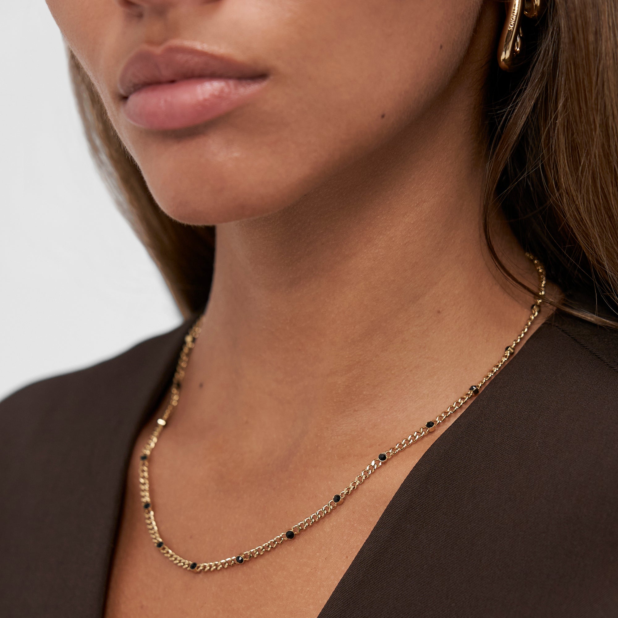 Eine Frau trägt die COPENHAGEN STUDIOS Halskette - Glittery necklace by Copenhagen Studios und passende Ohrringe, bekleidet mit einem dunkelbraunen Oberteil.