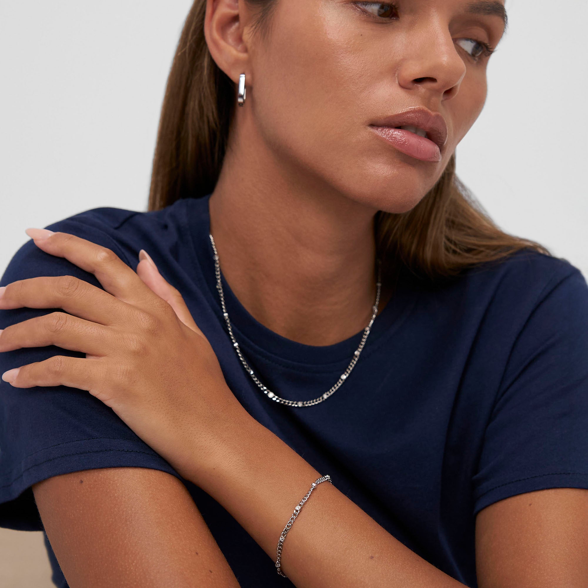Frau in einem navyfarbenen T-Shirt, gestylt mit Silberschmuck: die COPENHAGEN STUDIOS Halskette - Glittery necklace by Copenhagen Studios, plus passendem Armband und Reifohrringen, mit Blick zur Seite.