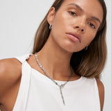 Frau in einem weißen ärmellosen Top trägt silberne Ohrringe und die COPENHAGEN STUDIOS Halskette - Edgy Necklace by Copenhagen Studios und blickt mit urbaner Ästhetik in die Kamera.