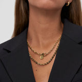 Eine Person in einem schwarzen Blazer trägt zwei übereinanderliegende Goldketten, darunter die COPENHAGEN STUDIOS Halskette - Edgy Necklace by Copenhagen Studios, sowie goldene Creolen - ein mühelos urbaner, von der Ästhetik inspirierter Look.