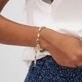 Das COPENHAGEN STUDIOS Armband - Edgy Bracelet von Copenhagen Studios mit seinem modernen goldenen Design passt perfekt zu einem weißen Oberteil und einer blauen strukturierten Hose für einen mühelos stilvollen Look.