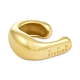 Der COPENHAGEN STUDIOS Ear Cuff - Organics von Copenhagen Studios zeichnet sich durch ein klobiges Golddesign mit glatter, glänzender Oberfläche, einem eingravierten Branding an der Seite und einem minimalistischen Stil aus.