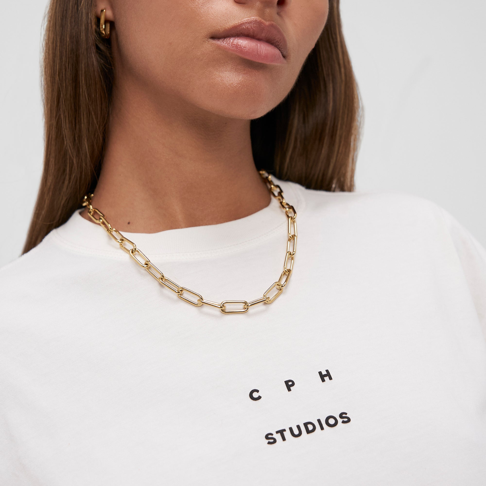 Eine Frau trägt das COPENHAGEN STUDIOS Halskette - Bold Set von Copenhagen Studios und ein weißes T-Shirt mit dem Aufdruck "COPENHAGEN STUDIOS".