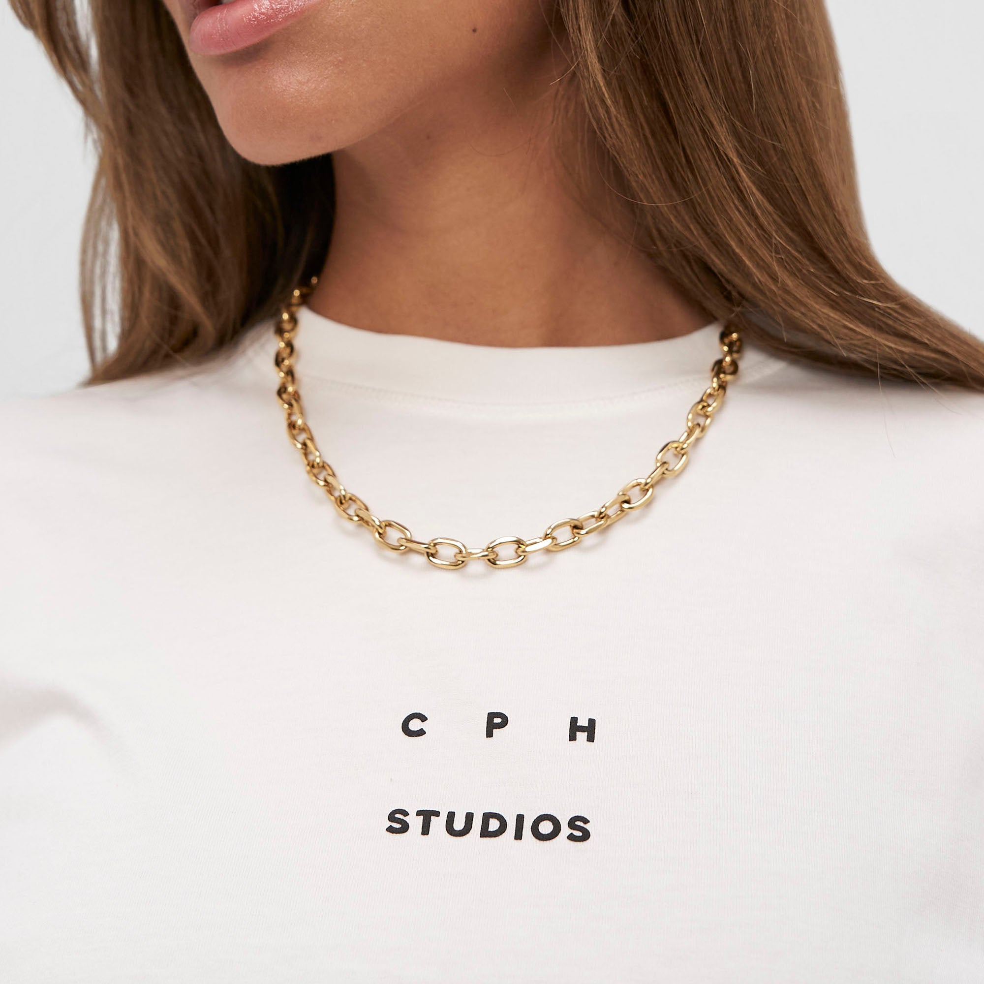 Frau trägt eine klobige goldene COPENHAGEN STUDIOS Halskette - Basic Chains und ein weißes Copenhagen Studios T-Shirt.