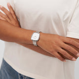 Person, die ein weißes Copenhagen Studios T-Shirt und die Copenhagen Studios Armbanduhr - Curved Watch mit über dem Oberkörper verschränkten Armen trägt.