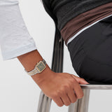 Eine Person im Business-Outfit sitzt auf einem Stuhl und trägt die Copenhagen Studios Armbanduhr - Vintage Watch - ein klassisches Accessoire, das ihrem Look Raffinesse verleiht.