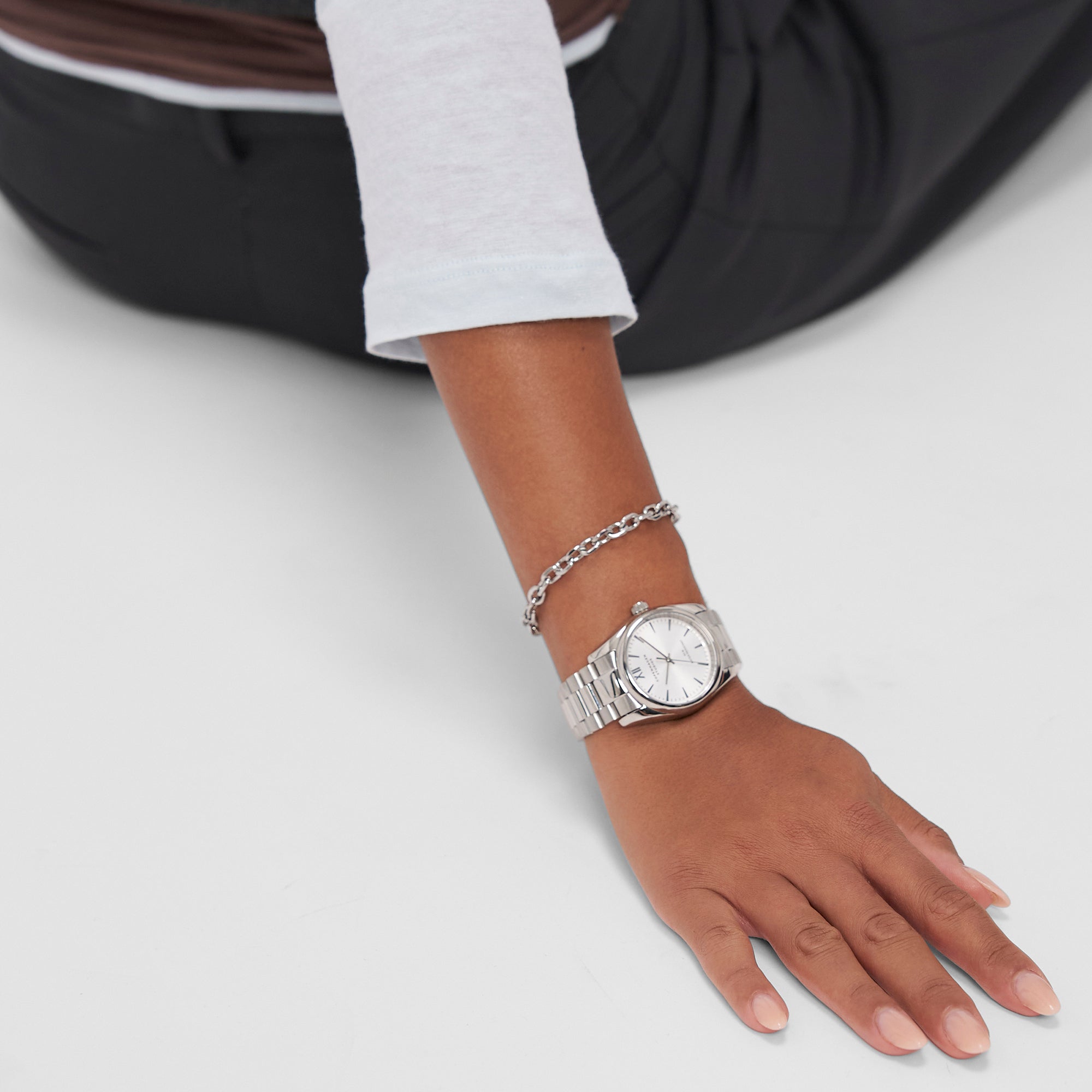 Eine Person, die die COPENHAGEN STUDIOS Armbanduhr - Round Watch by Copenhagen Studios und ein Kettenarmband trägt, stützt ihre Hand auf eine weiße Fläche und präsentiert zeitloses Design.