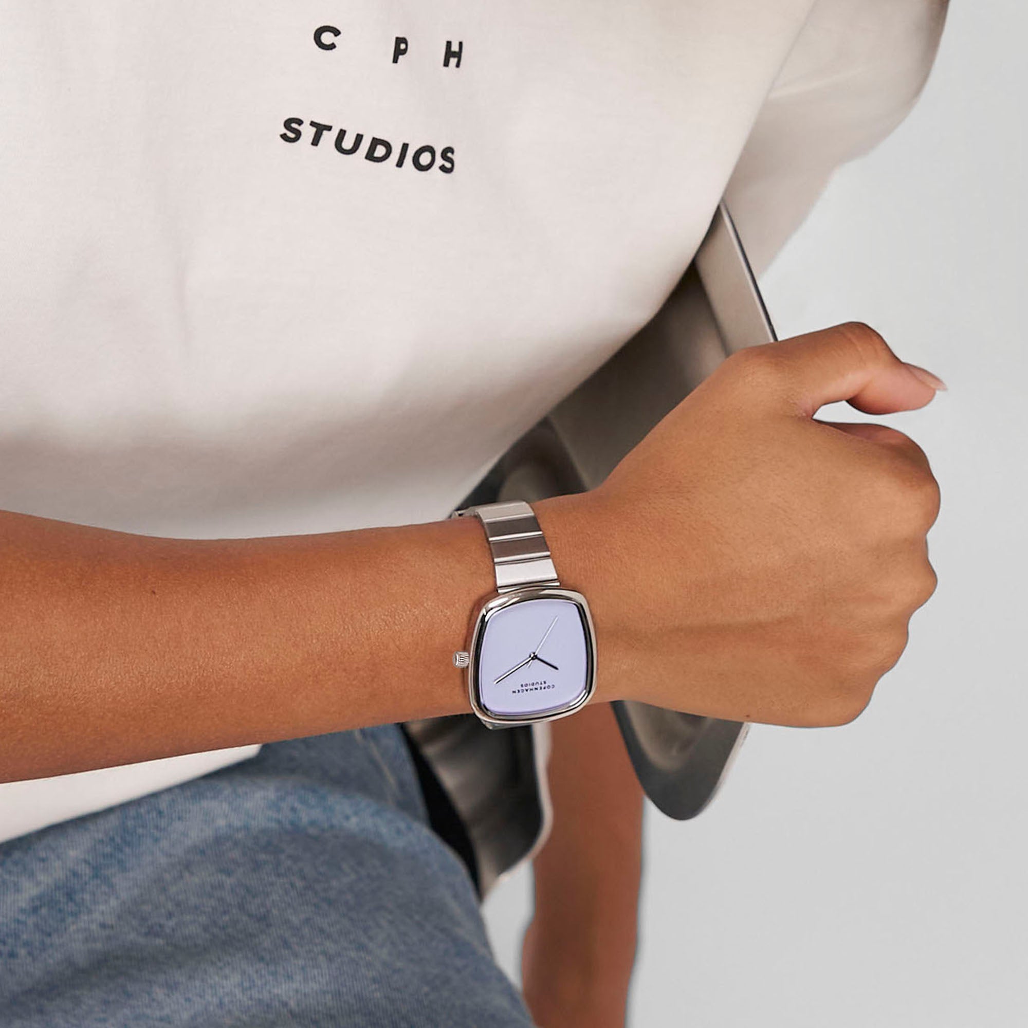 Person, die eine Copenhagen Studios Curved Watch und ein Copenhagen Studios-T-Shirt trägt und ein graues Tablet in der Hand hält.